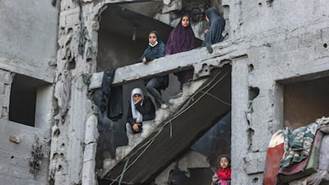 Donne e bambini palestinesi si trovano nella scalinata di un edificio gravemente danneggiato. AFP