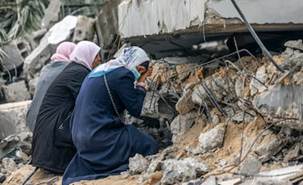 Le donne palestinesi si stringono per un punto in cui si ritiene che un parente sia intrappolato sotto i detriti, a Rafah. AFP